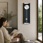 Standuhren.com 🕰️ AMS Pendel-Funkwanduhr in Schwarz mit Aluminium-Details, hängend in einem modernen Wohnzimmer.